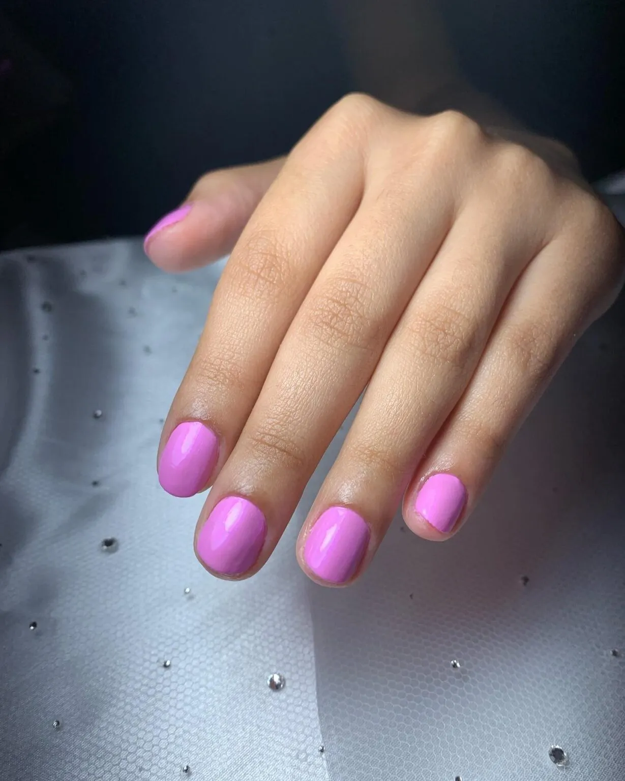 Unhas arredondadas com esmalte rosa brilhante.