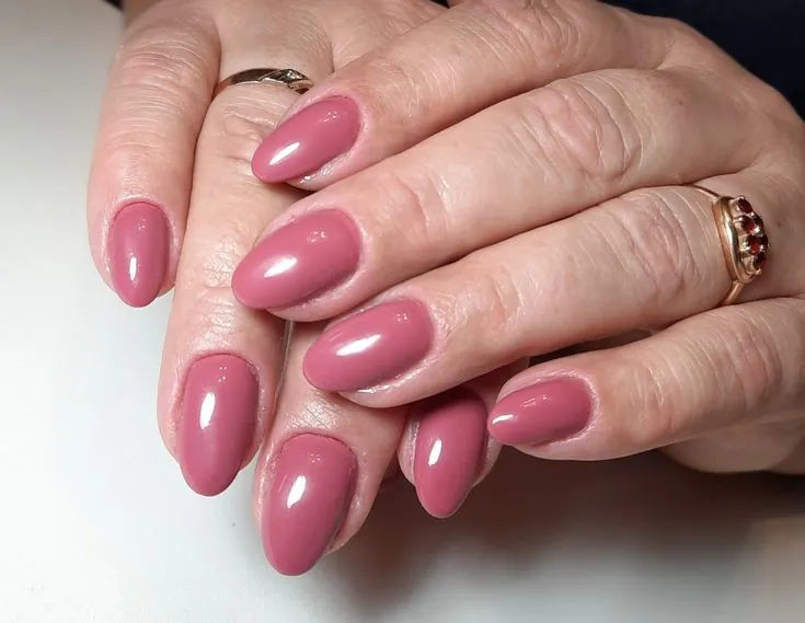 Mãos maduras com unhas amendoadas em esmalte rosa.