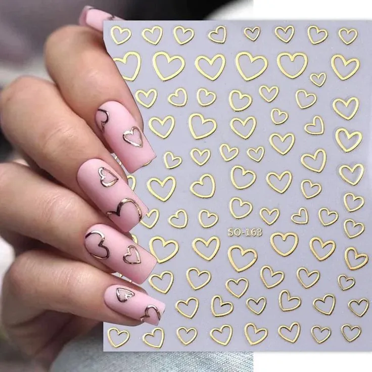 Unhas decoradas com corações em 3D dourados sobre esmalte rosa