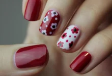Unhas curtas com esmalte vermelho e decoração floral em branco e vermelho, mostrando estilo e delicadeza.
