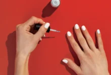 Mãos femininas esmaltando unhas brancas sobre fundo vermelho