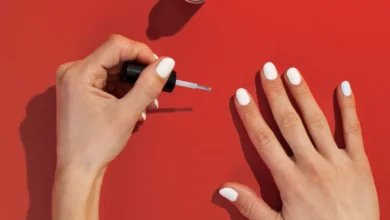 Mãos femininas esmaltando unhas brancas sobre fundo vermelho