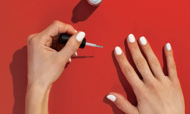 Mãos femininas esmaltando unhas brancas sobre fundo vermelho