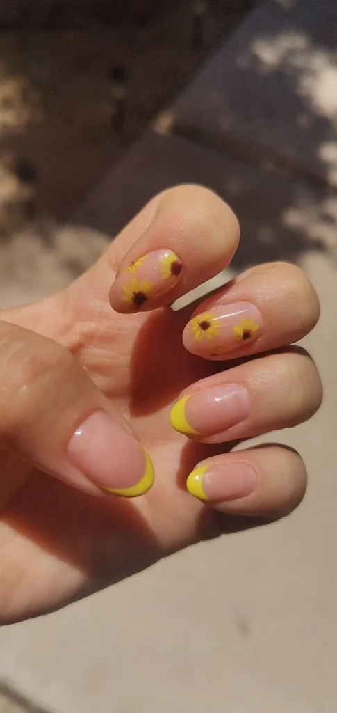 Unhas decoradas com flores amarelas delicadas e pontas amarelas vibrantes