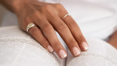 Mão feminina com francesinha delicada em tom nude e glitter, segurando um livro aberto.
