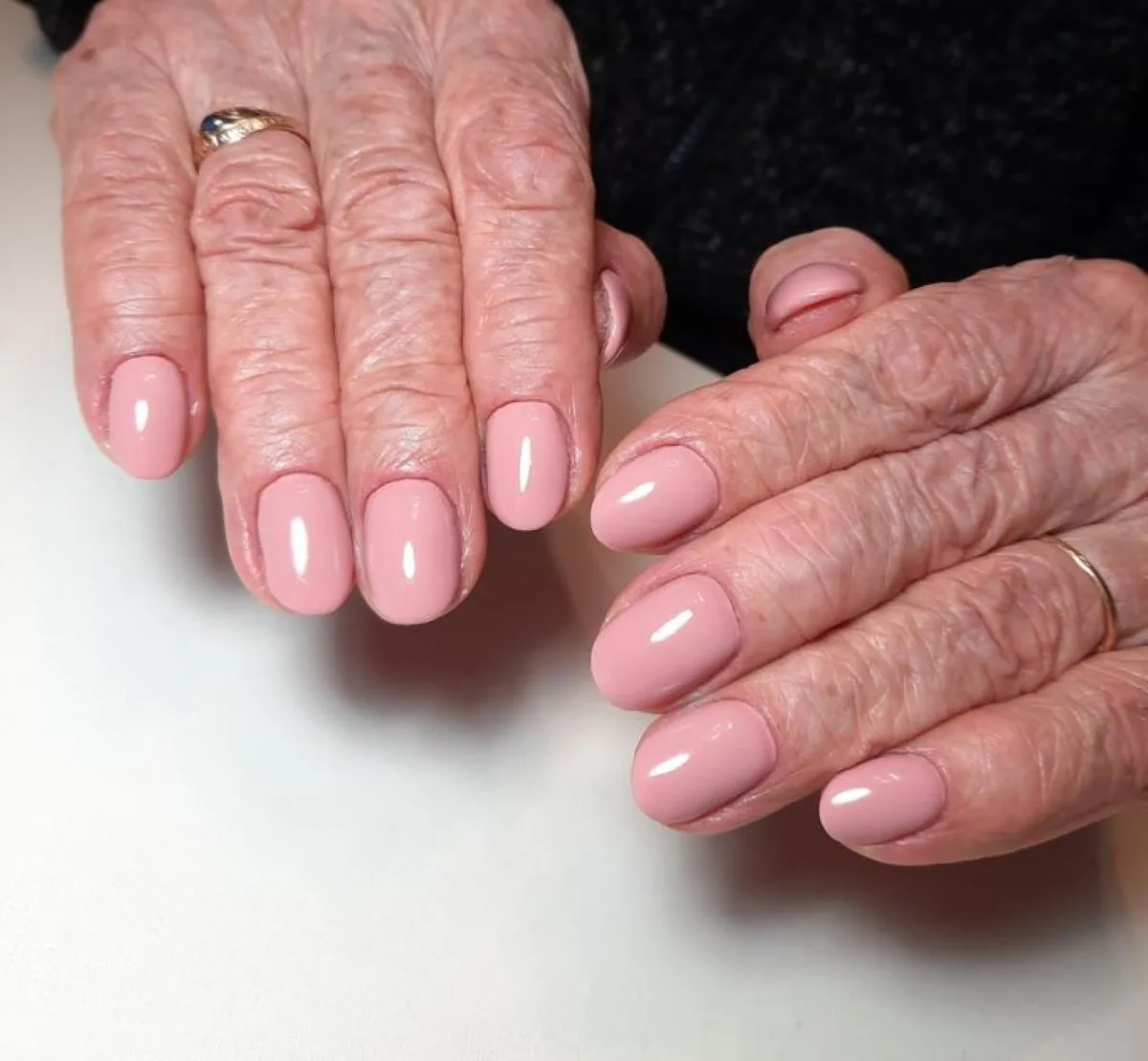 Unhas rosadas elegantes em mãos de mulher madura com acabamento brilhante