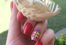 Unhas vermelhas com unha decorada em colorida segurando um mini chapéu de palha