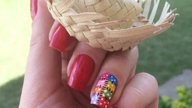 Unhas vermelhas com unha decorada em colorida segurando um mini chapéu de palha