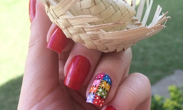 Unhas vermelhas com unha decorada em colorida segurando um mini chapéu de palha