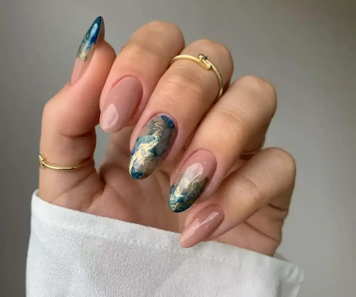 Unhas redondas decoradas com esmalte nude e detalhes em azul e dourado