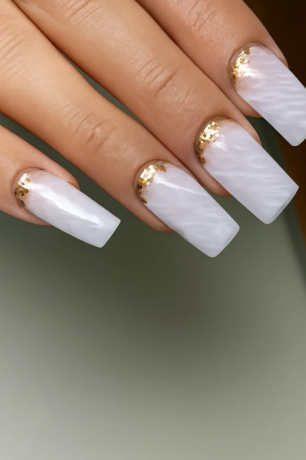 Nail art com efeito marmorizado branco e folhas douradas nas unhas quadradas.