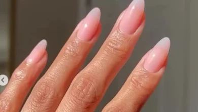 Unhas com esmalte em degradê rosa suave, formato amendoado, adornadas com anéis dourados minimalistas.