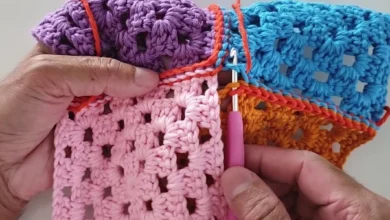 Mãos segurando peças coloridas de crochê unidas com ponto delicado usando agulha