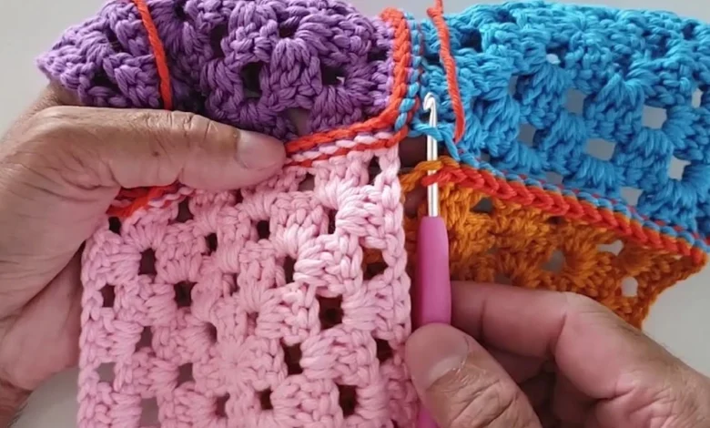 Mãos segurando peças coloridas de crochê unidas com ponto delicado usando agulha