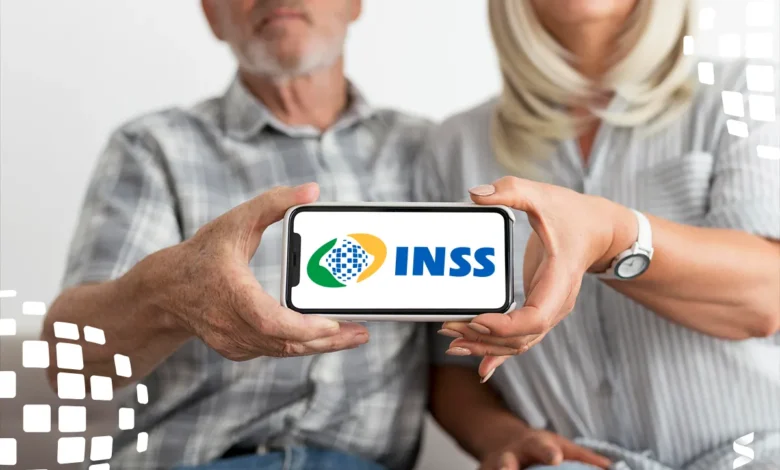 Casal de idosos segurando um celular com o logo do INSS, simbolizando a consulta de valores a receber.