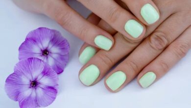 Unhas curtas pintadas de verde leitoso ao lado de flores roxas