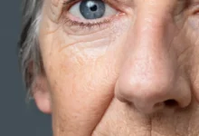 Close-up do rosto de uma mulher idosa, com foco nas linhas de expressão e na textura da pele, simbolizando os efeitos do envelhecimento.