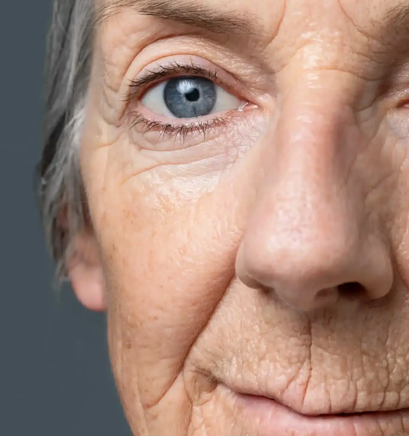 Close-up do rosto de uma mulher idosa, com foco nas linhas de expressão e na textura da pele, simbolizando os efeitos do envelhecimento.