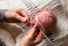 Mãos segurando agulha e fio rosa enquanto fazem crochê