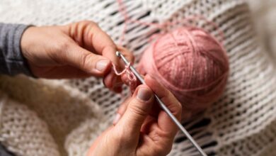 Mãos segurando agulha e fio rosa enquanto fazem crochê