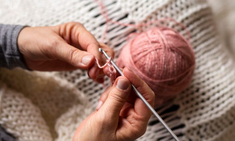 Mãos segurando agulha e fio rosa enquanto fazem crochê