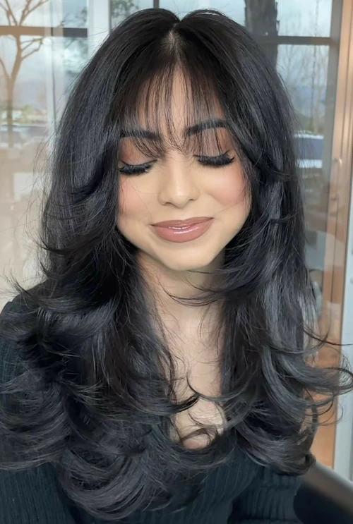 Mulher com corte butterfly e franja moderna, cabelos volumosos e estilo elegante.