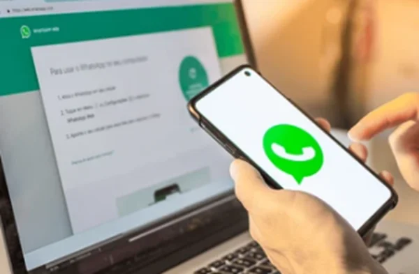 Pessoa usando o WhatsApp Web em um laptop e smartphone para criar figurinhas