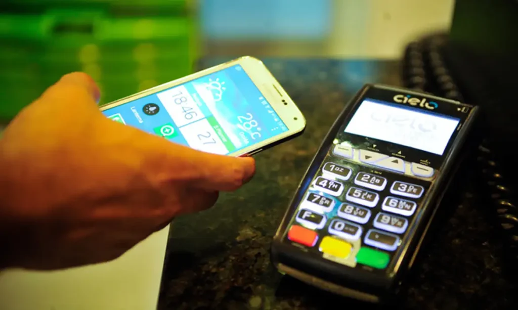 Pessoa realizando pagamento por aproximação com celular em máquina da Cielo