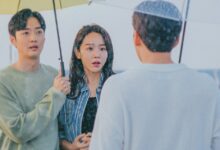 Cena do dorama De Volta às Raízes com casal debaixo de guarda-chuva encarando homem na chuva