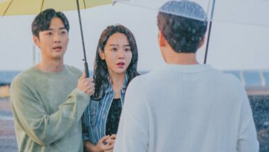Cena do dorama De Volta às Raízes com casal debaixo de guarda-chuva encarando homem na chuva