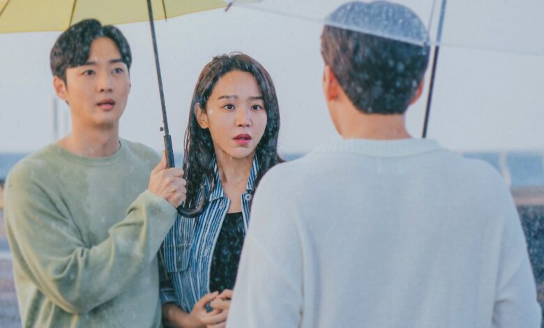 Cena do dorama De Volta às Raízes com casal debaixo de guarda-chuva encarando homem na chuva