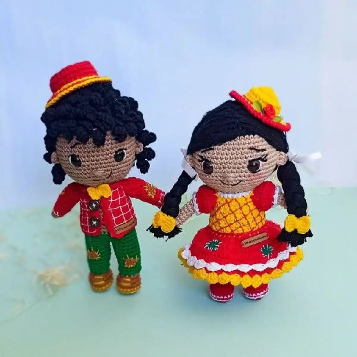 Bonecos de amigurumi caipiras com roupas coloridas, feitos em crochê, representando casal típico de festa junina.