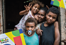 Família sorrindo na porta de casa segurando o cartão do Bolsa Família