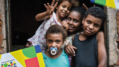 Família sorrindo na porta de casa segurando o cartão do Bolsa Família
