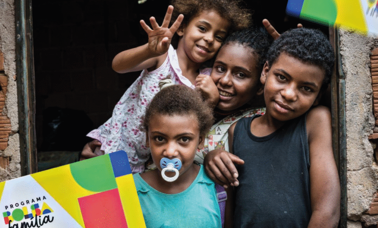 Família sorrindo na porta de casa segurando o cartão do Bolsa Família
