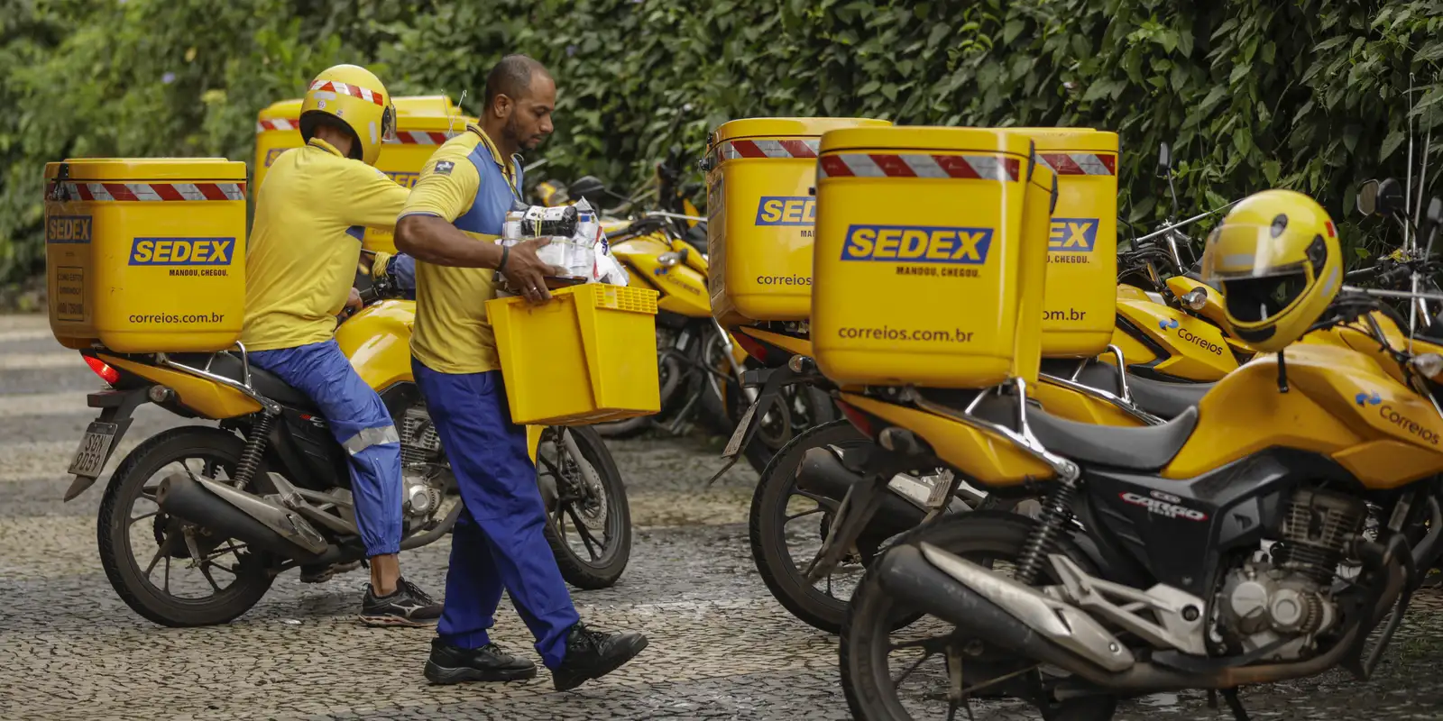 Entregadores dos Correios utilizando motos com caixas de SEDEX, refletindo a operação logística da empresa.