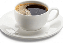 Xícara branca com café preto quente servida em pires sobre fundo claro