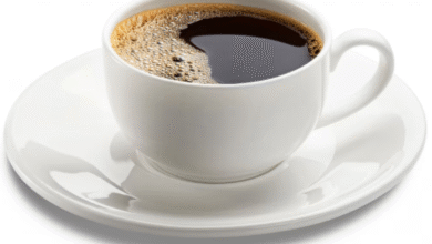 Xícara branca com café preto quente servida em pires sobre fundo claro