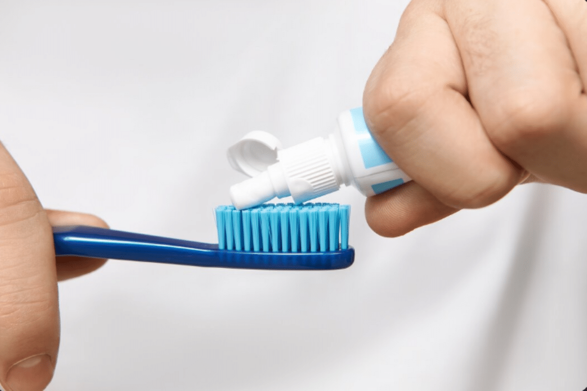 Pessoa aplicando creme dental em uma escova de dentes azul