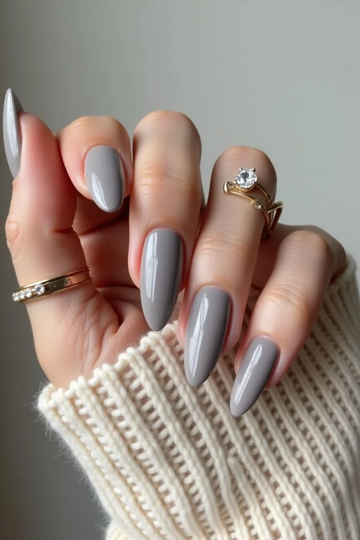 Imagem de unhas com esmalte cinza pardo e anéis delicados.