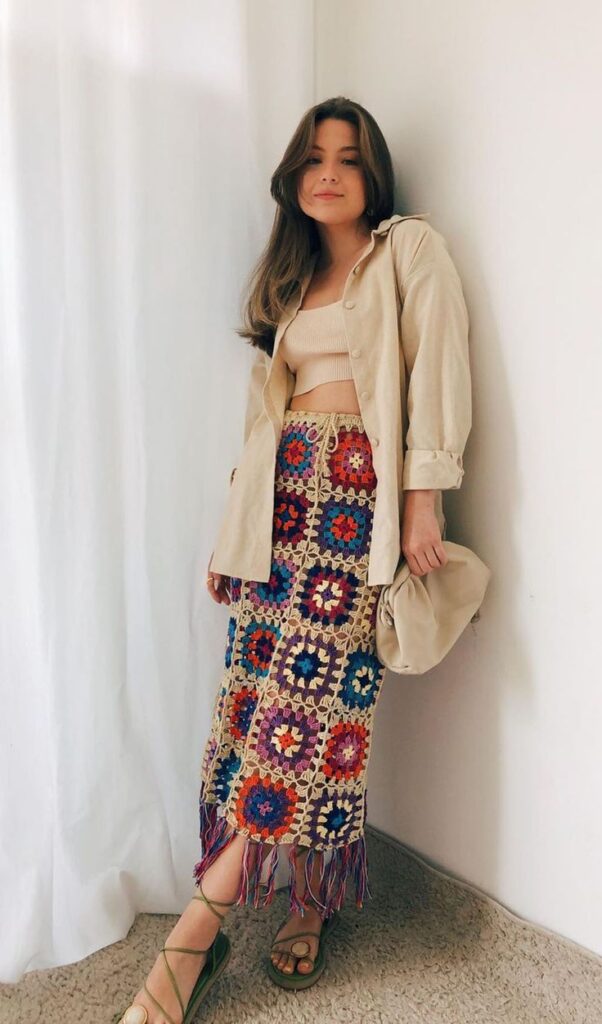 Mulher usando saia midi de crochê colorida com camisa bege e sandália no estilo casual