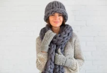 Mulher com cachecol grosso e luvas de crochê, utilizando acessórios de inverno em tons terrosos.