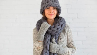 Mulher com cachecol grosso e luvas de crochê, utilizando acessórios de inverno em tons terrosos.