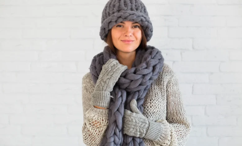 Mulher com cachecol grosso e luvas de crochĂȘ, utilizando acessĂłrios de inverno em tons terrosos.