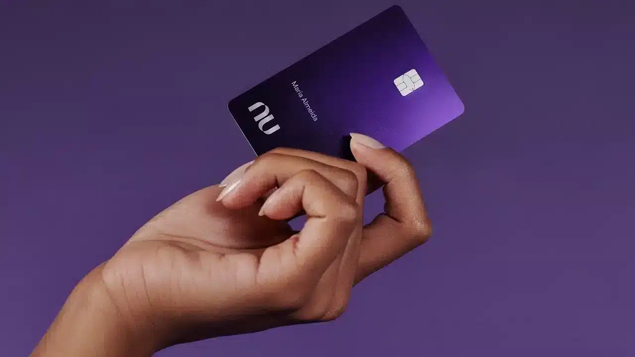 Cartão de crédito Nubank Ultravioleta em mãos com fundo roxo, representando a exclusividade e inovação do produto.