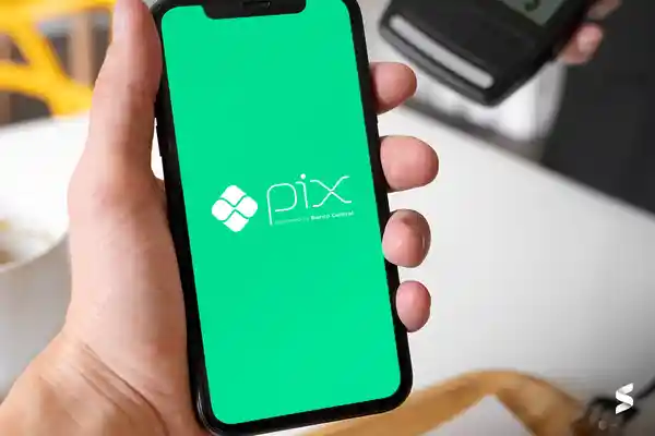 Pessoa usando o celular com o logo do Pix na tela, representando a utilização do Pix Automático para pagamentos rápidos.
