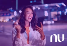 Mulher sorrindo ao usar o smartphone à noite, com luzes de cidade ao fundo, representando a inovação do Nubank.