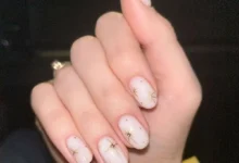 Unhas curtas e naturais com desenhos delicados e brilho dourado, estilo clean girl.