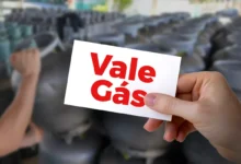 Cartão do Vale Gás sendo segurado em meio a botijões de gás, representando o programa de auxílio social.