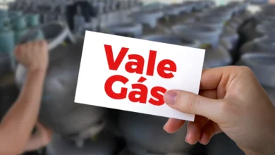 Cartão do Vale Gás sendo segurado em meio a botijões de gás, representando o programa de auxílio social.